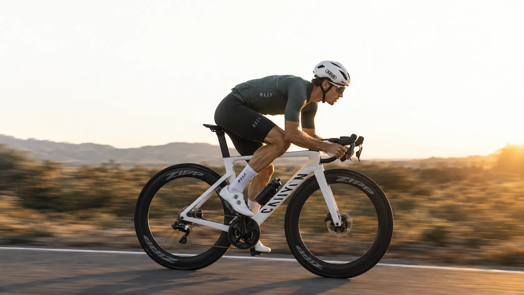 A cyclist riding a time-trial bike along a desert road at sunrise